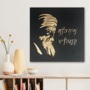 以下が含まれることがあります： 黒のキャンバスに、金色のシルエットで描かれた、ひげを生やしたターバンを巻いた男性。"ਮਾਣੁ ਨਾਮੁ ਵਡਿਆਈ"という文字が金色の文字で書かれている。