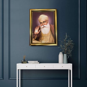 May include: A framed portrait of a man with a white beard and turban, wearing a yellow robe. The portrait is set against a purple background and framed in gold.