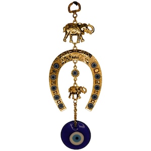 May include: Gold horseshoe charm with a blue evil eye charm hanging from it. The horseshoe is decorated with blue evil eyes and has a small gold elephant charm hanging from it.