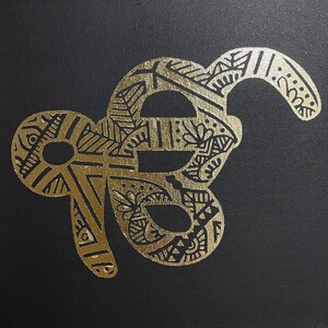 Op de afbeelding: Een gouden slangontwerp met ingewikkelde patronen op een zwarte achtergrond.