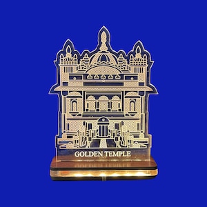 Può includere: Luce notturna a LED del Golden Temple. La struttura in acrilico, con dettagli architettonici, reca la scritta "GOLDEN TEMPLE". Poggia su una base in legno con LED integrati, su sfondo blu.