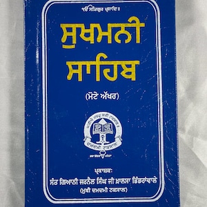 May include: A blue book with the title "Sukhamani Sahib" in gold lettering. The book is published by the "Damdami Taksal" and features a white seal with a book and a sword.