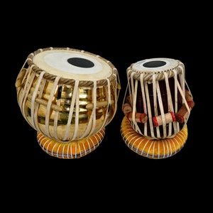 Puede incluir: Dos tambores tabla indios, uno con acabado dorado y el otro con acabado marrón. Ambos tambores tienen una parte superior de cuero blanco y están decorados con correas marrones y rojas.