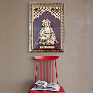 May include: A framed wooden artwork featuring a seated figure with a halo, set against a dark wood background. The frame is gold with intricate detailing, and text is visible at the top and bottom. A red chair with a book is in the foreground.