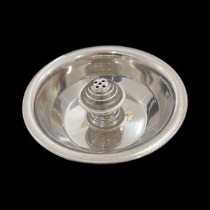 Peut inclure: Un brûleur d'encens argenté avec une structure centrale à plusieurs niveaux, percée de petits trous en haut. Le brûleur est placé dans un bol peu profond, avec un motif floral doré sur la base.