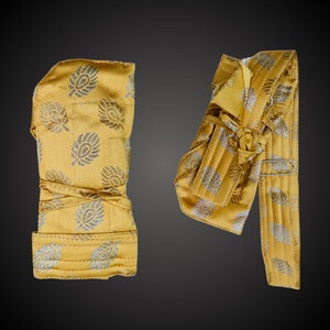 May include: Two gold fabric sashes with a silver floral pattern. The sashes are folded and tied in different ways.