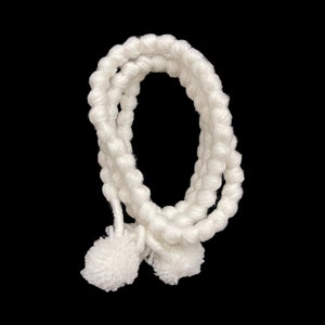 May include: White crocheted cord with two fluffy pom-poms at the ends.
