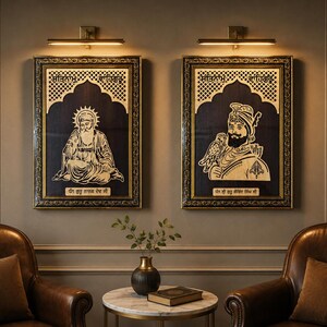 May include: Two rectangular framed wall art pieces featuring gold-toned portraits of Sikh figures on a dark background. Each frame includes intricate gold detailing and Gurmukhi script text at the top and bottom, illuminated by individual wall lights.