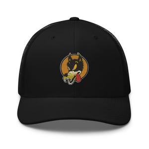 May include: A black trucker hat featuring a mesh back and a solid front panel. Centered on the front is a circular patch with an orange background, displaying a cartoon-style black wolf head with a red tongue, white teeth, and yellow eyes.