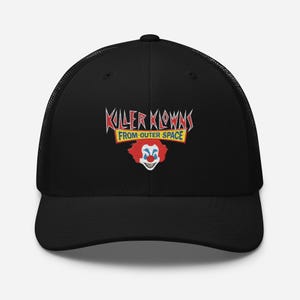 Puede incluir: Una gorra de camionero negra con parte trasera de malla y un gráfico frontal con el texto Killer Klowns From Outer Space en letras rojas y amarillas sobre una cara de payaso estilizada con pelo rojo y nariz roja.
