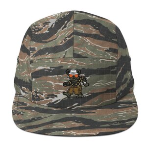 Könnte beinhalten: Eine Fünf-Panel-Kappe mit Tigerstreifen-Camouflage-Muster in Grün-, Braun- und Schwarztönen. Auf der Vorderseite befindet sich eine Stickerei eines Bären, der einen weißen Fischerhut, eine orangefarbene Sonnenbrille und ein Blumenhemd trägt.