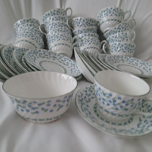 May include: A collection of white porcelain teacups, saucers, and bowls. The set features a blue floral pattern and a green trim. The teacups have handles, and the bowls have a spiral design. A complete tea set.