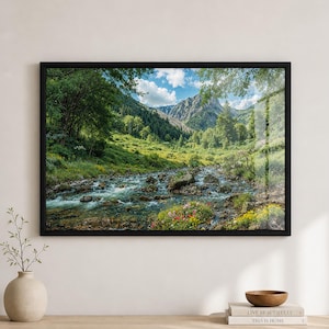 May include: A framed landscape print featuring a mountain stream flowing through a lush green valley. The artwork showcases a vibrant scene with trees, wildflowers, and a bright blue sky with clouds. The black frame adds a modern touch.