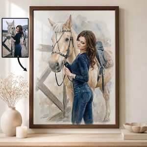 Puede incluir: Pintura a la acuarela de una mujer con cabello casta&ntilde;o largo y un caballo. La mujer lleva un top y vaqueros azul oscuro, sujetando las riendas del caballo. El caballo es de color marr&oacute;n claro con una silla de montar. La obra est&aacute; enmarcada en un marco de madera marr&oacute;n oscuro.