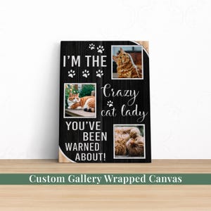 May include: A custom gallery-wrapped canvas with a black wood-look background. The canvas features three photos of cats and the text "I'M THE CRAZY CAT LADY YOU'VE BEEN WARNED ABOUT!" in white script and block letters. Paw prints are scattered throughout.