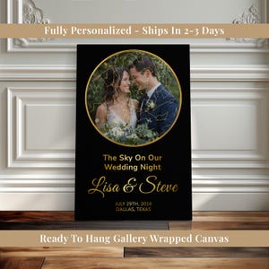 May include: Black canvas print featuring a couple's photo within a gold circle, overlaid with a star map. The text "The Sky On Our Wedding Night" and names "Lisa & Steve" are in gold script. Includes date and location.