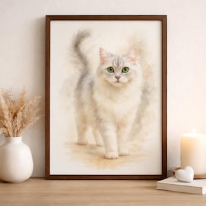 May include: Watercolor print of a fluffy white cat with gray accents and green eyes, framed in a dark brown wooden frame. The artwork is displayed on a wooden surface, with a vase of dried flowers and a lit candle nearby. The cat is the focal point.