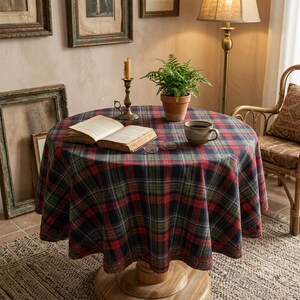 May include: A round table covered with a red, green, and navy blue plaid tablecloth. On the table sits an open hardback book, a small potted green fern in a terracotta pot, a brass candlestick with a candle, and a ceramic mug with glasses.