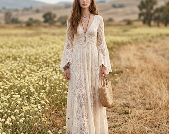 May include: A floor-length cream-colored lace dress featuring long bell sleeves, a deep V-neckline, and a fitted bodice that transitions into a flowing skirt. The garment is accessorized with a long pendant necklace and a woven straw handbag.
