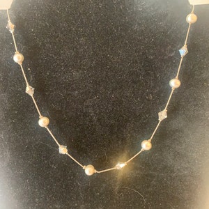 May include: Delicate gold-toned necklace featuring alternating faux pearls and clear, faceted crystals. The necklace is displayed against a black background, highlighting the jewelry's elegant design. A classic accessory for special occasions.