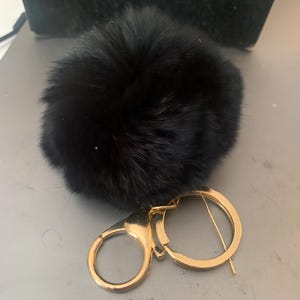 May include: A black fluffy pom pom keychain with a gold metal key ring.