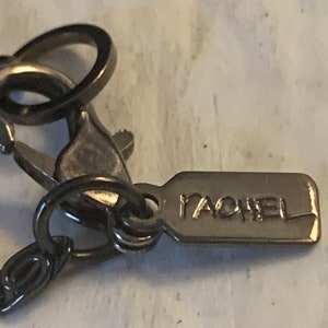 May include: Close-up of a silver-toned necklace clasp with a small tag that reads "RACHEL".