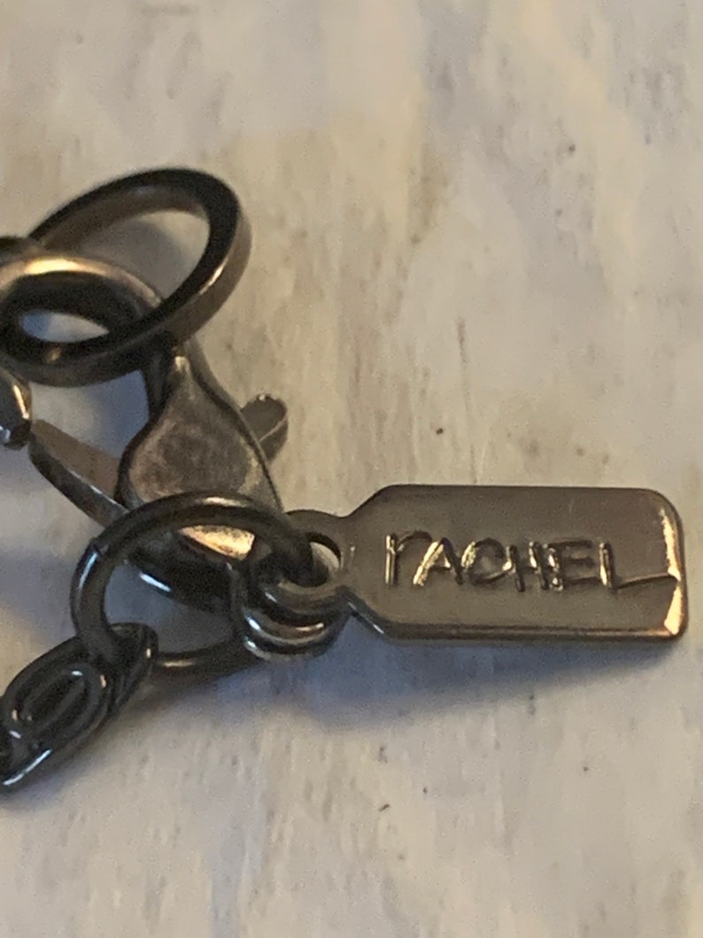 May include: Close-up of a silver-toned necklace clasp with a small tag that reads "RACHEL".