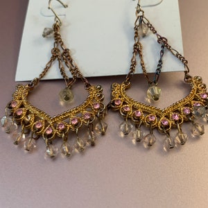 Könnte beinhalten: Ein Paar goldfarbene Ohrhänger mit rosa und klaren Kristall-Akzenten. Die Ohrringe haben ein zartes Ketten-Design und sind mit "Mixit." beschriftet.