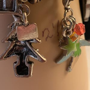 Puede incluir: Primer plano de una pulsera de plata con varios abalorios. Los abalorios incluyen un &aacute;rbol de Navidad, una estrella con detalles verdes y naranjas, y un peque&ntilde;o abalorio rectangular. La pulsera tambi&eacute;n presenta una perla y elementos met&aacute;licos decorativos.