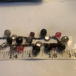 May include: A black beaded necklace with clear, pink, and gray beads. The necklace is approximately 15 inches long.