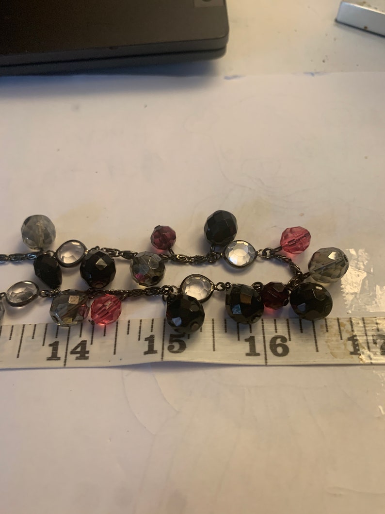 May include: A black beaded necklace with clear, pink, and gray beads. The necklace is approximately 15 inches long.