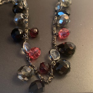 May include: A silver chain necklace with black, clear, and pink faceted glass beads. The beads are of various sizes and shapes.