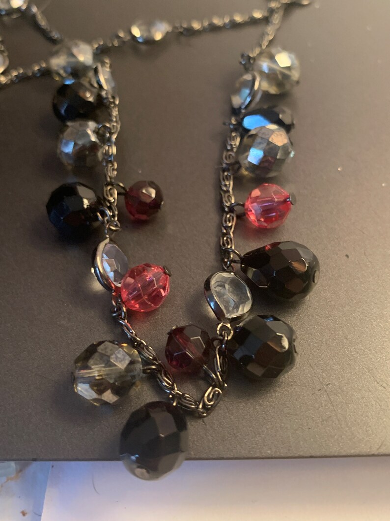 May include: A silver chain necklace with black, clear, and pink faceted glass beads. The beads are of various sizes and shapes.