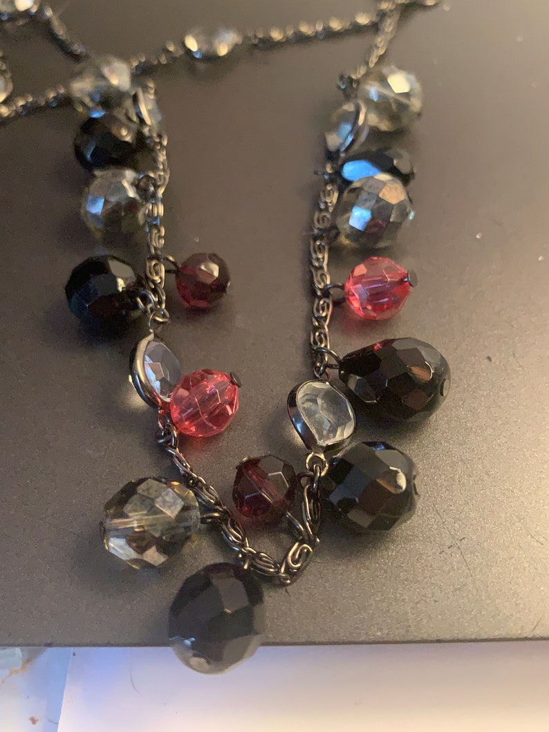 May include: A black chain necklace with dangling beads in various colors, including black, gray, pink, and red.