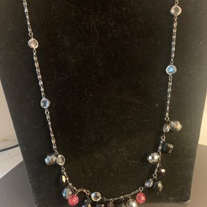 May include: A silver chain necklace with black, clear, and pink faceted beads. The beads dangle from the chain, creating a layered look.