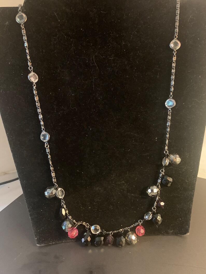 May include: A silver chain necklace with black, clear, and pink faceted beads. The beads dangle from the chain, creating a layered look.