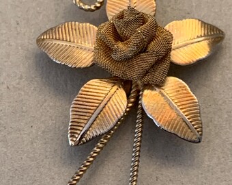 May include: A gold-toned brooch featuring a rose with leaves and twisted wire accents.