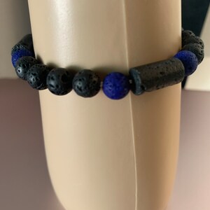 Puede incluir: Pulsera de cuentas negras y azules con cuentas de roca volcánica y una cuenta de roca volcánica negra más grande.