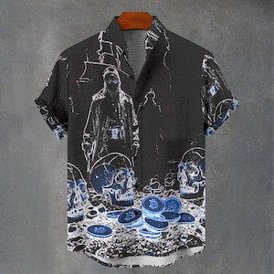 Könnte beinhalten: Schwarzes Kurzarmhemd mit einem einzigartigen Design, das eine Figur, Totenköpfe und Bitcoin-Symbole in Weiß und Blau zeigt. Das Hemd hat eine Brusttasche und einen klassischen Kragen, ideal für Freizeitkleidung.