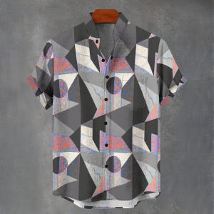 May include: Short-sleeved shirt with a geometric design in grey, black, white, orange and blue. The shirt is hanging on a wooden hanger. The shirt has a classic collar and a single chest pocket. The background is grey. The shirt is buttoned up.