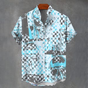 May include: Short-sleeved button-up shirt with a skull and checkerboard pattern in shades of blue, gray, and white. The shirt is hanging on a wooden hanger against a gray background.