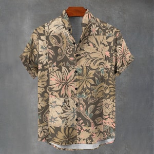 Pode incluir: Camisa de manga curta com estampa floral em tons de castanho, bege, rosa e azul-petróleo. A camisa está pendurada em um cabide de madeira sobre um fundo cinza. O design da camisa apresenta um patchwork de motivos florais e paisley.