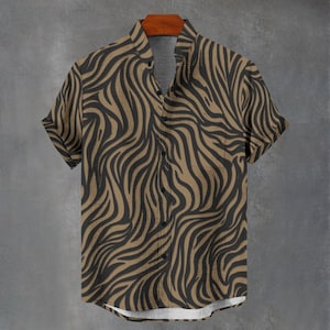 May include: A short-sleeved button-down shirt featuring a tan and black wavy zebra-like pattern. The shirt has a mandarin collar, a front button placket with dark buttons, and a single chest pocket on the left side, displayed on a hanger.