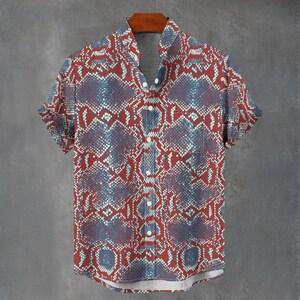 Peut inclure: Une chemise à manches courtes boutonnée avec un motif répétitif de peau de serpent dans des tons rouge foncé, bleu marine et blanc. La chemise présente un col classique, une poche poitrine sur le côté gauche et des boutons blancs sur le devant.