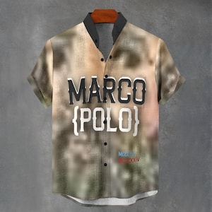 Op de afbeelding: Een shirt met korte mouwen met een wazig, abstract patroon in tinten beige, bruin en beige. Het shirt heeft de tekst "MARCO {POLO}" in zwart en wit, met extra tekst onderaan. De kraag is zwart.