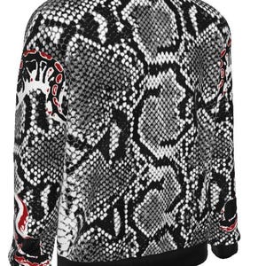 May include: A long-sleeved sweatshirt featuring a black, white, and grey snakeskin pattern across the entire garment. The design includes solid black trim at the crew neckline, cuffs, and hem, with distinct red and white abstract accents on the sleeves.