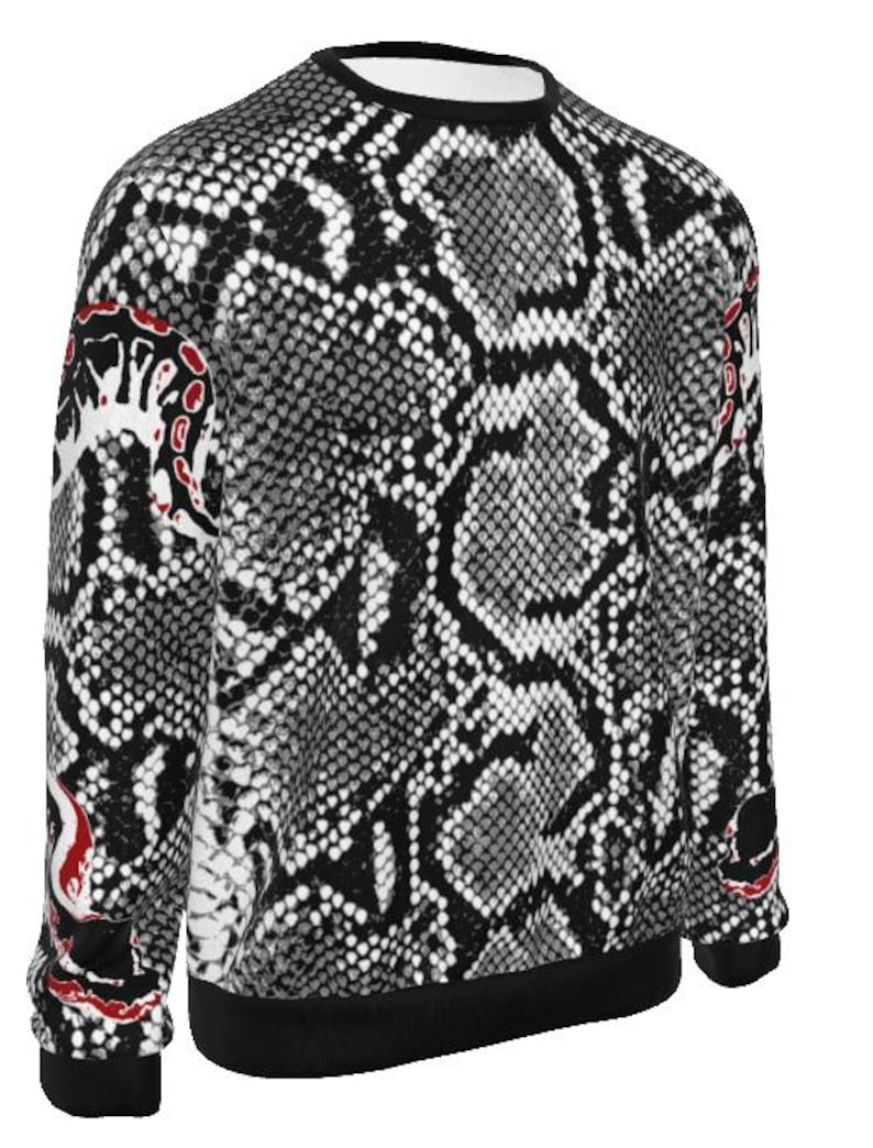 May include: A long-sleeved sweatshirt featuring a black, white, and grey snakeskin pattern across the entire garment. The design includes solid black trim at the crew neckline, cuffs, and hem, with distinct red and white abstract accents on the sleeves.
