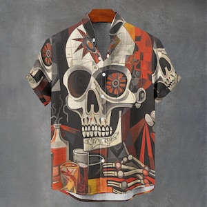May include: Short-sleeved button-up shirt with a skull design. The shirt features a large skull graphic with geometric shapes and a color palette of black, red, orange, and white. The shirt is hanging on a wooden hanger.