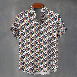 May include: A short-sleeved button-down shirt featuring a repeating geometric pattern of black, white, red, yellow, and blue triangles. The shirt has a classic collar, a front button placket with dark buttons, and a straight hemline.