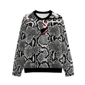 Könnte beinhalten: Ein langärmeliges Sweatshirt mit einem schwarz-weiß-grauen Schlangenhautmuster auf dem gesamten Kleidungsstück. Eine stilisierte Schlangengrafik mit roten und schwarzen Akzenten befindet sich im oberen Brust- und Schulterbereich, mit einem schwarzen Rundhalsausschnitt.